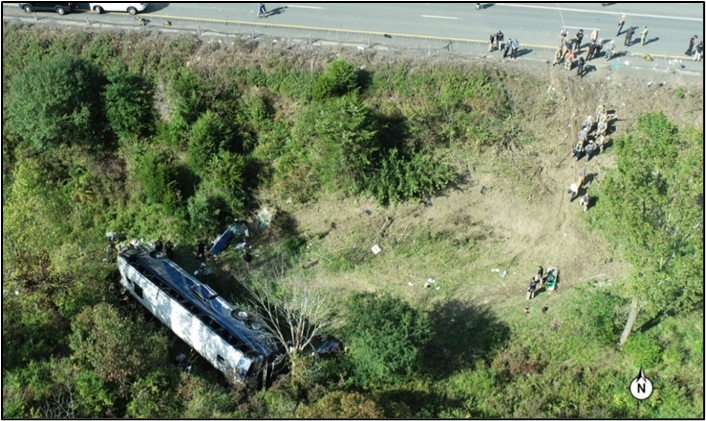 Aerial view of the motorcoach at final rest on its left side at the bottom of the median. 